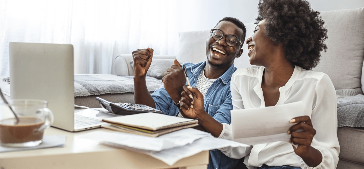 African-American man and woman smiling and reviewing documents with laptop and calculator