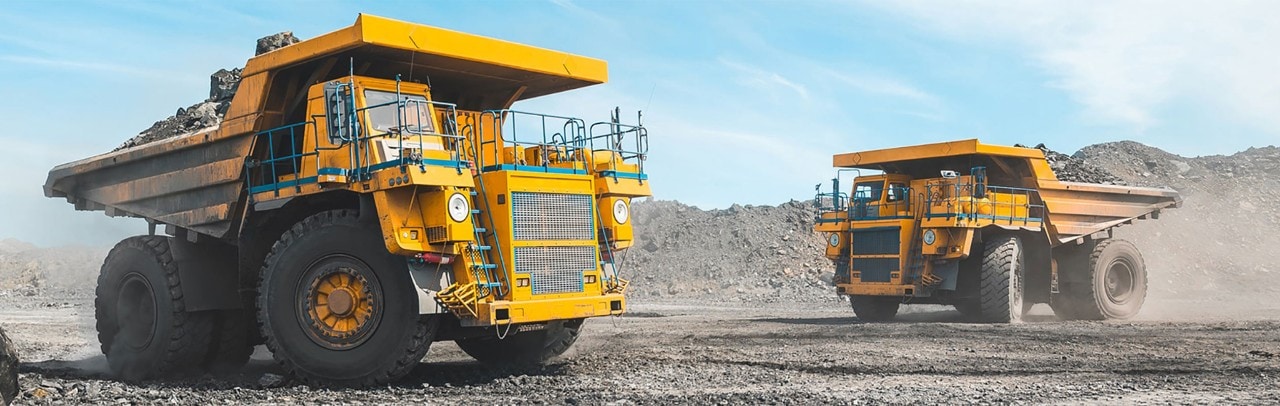 Two large construction dump trucks driving on rocky surface
