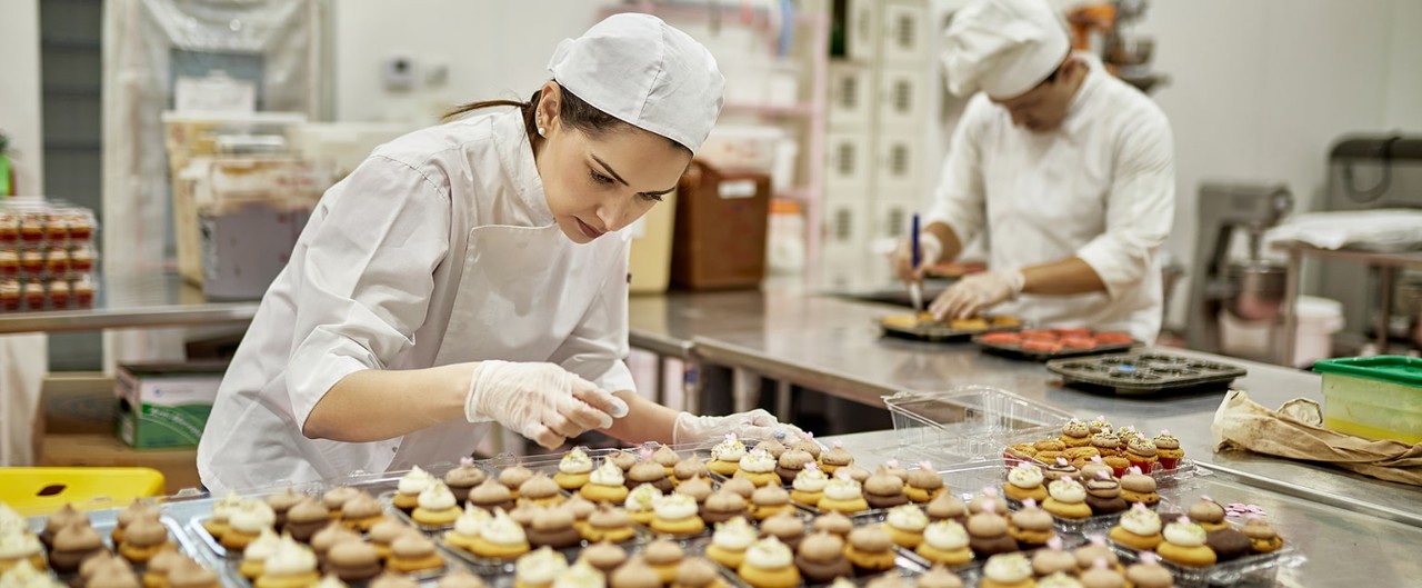 Female professional baker icing large order of cupcakes