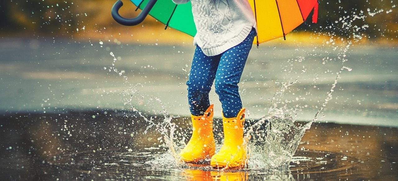 Child with yellow rainboots jumps in puddle 