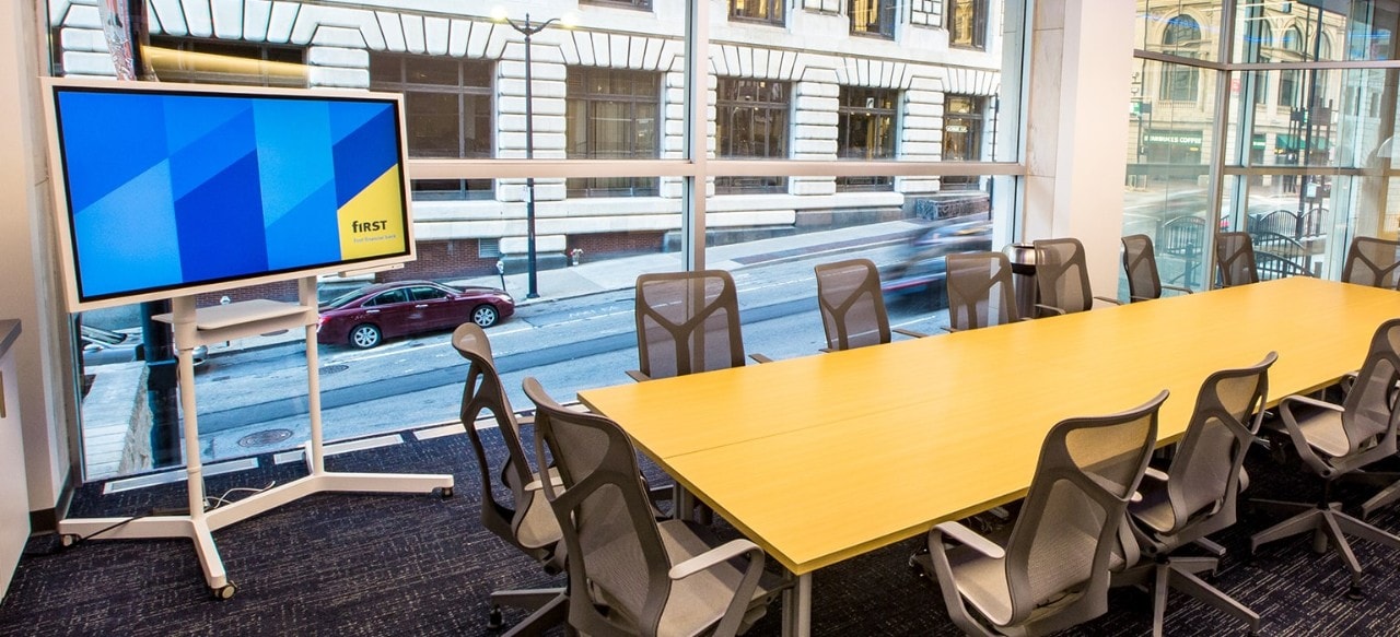 A board room with empty seats and a tv screen for projecting.
