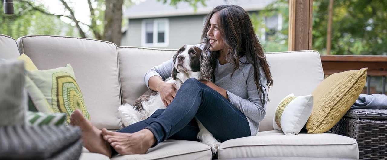 Woman snuggling with dog on outdoor patio sofa