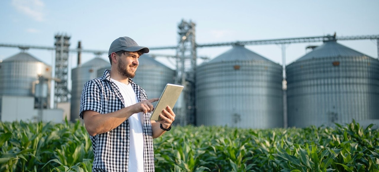 Farmer using tablet in front of grain elevators