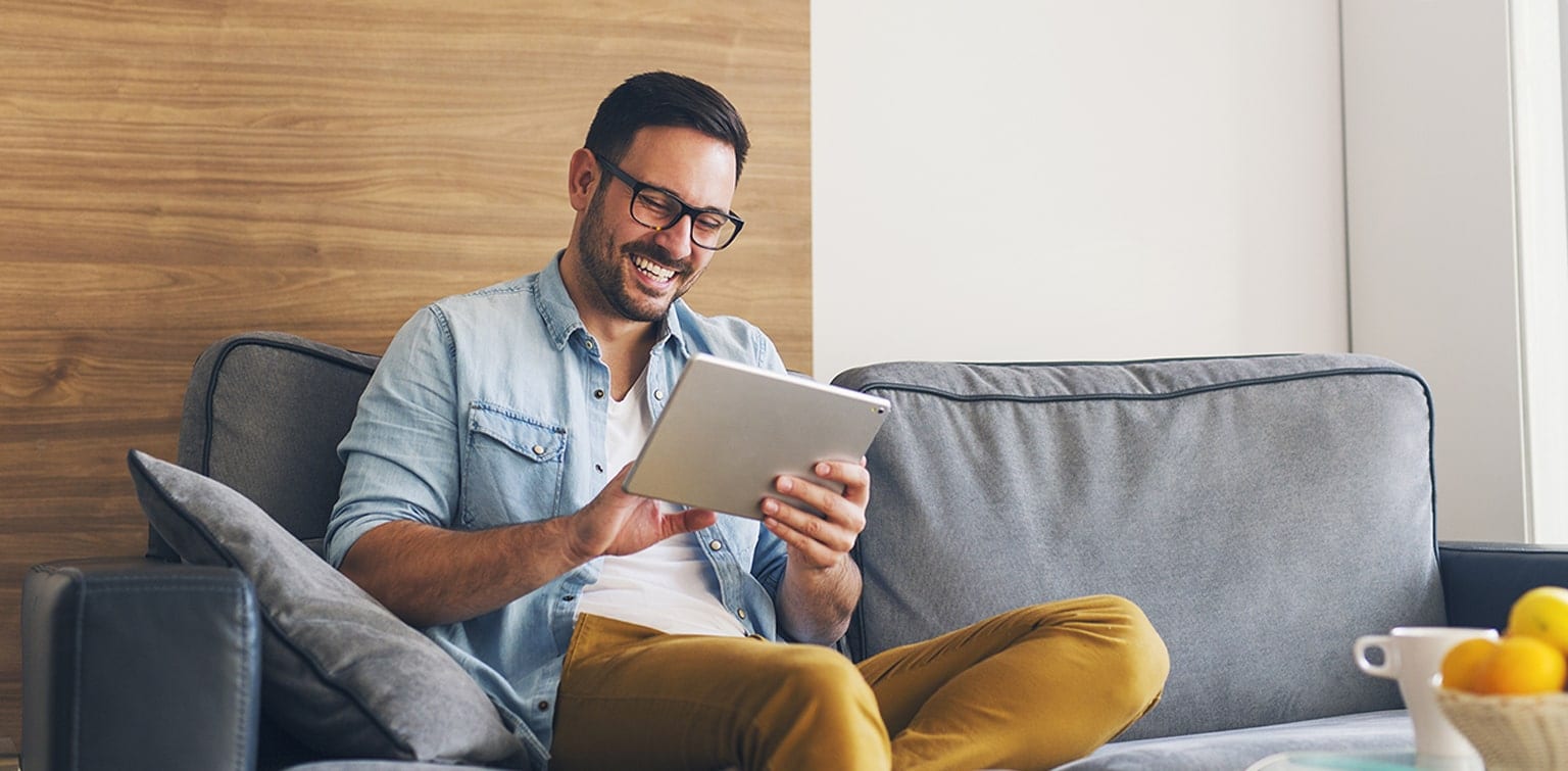 Happy man sitting on sofa looking at tablet