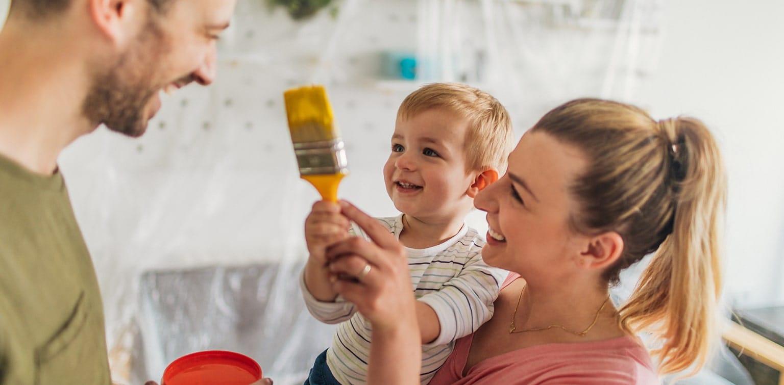 Mother holding child who’s ready to paint father yellow with a paint brush