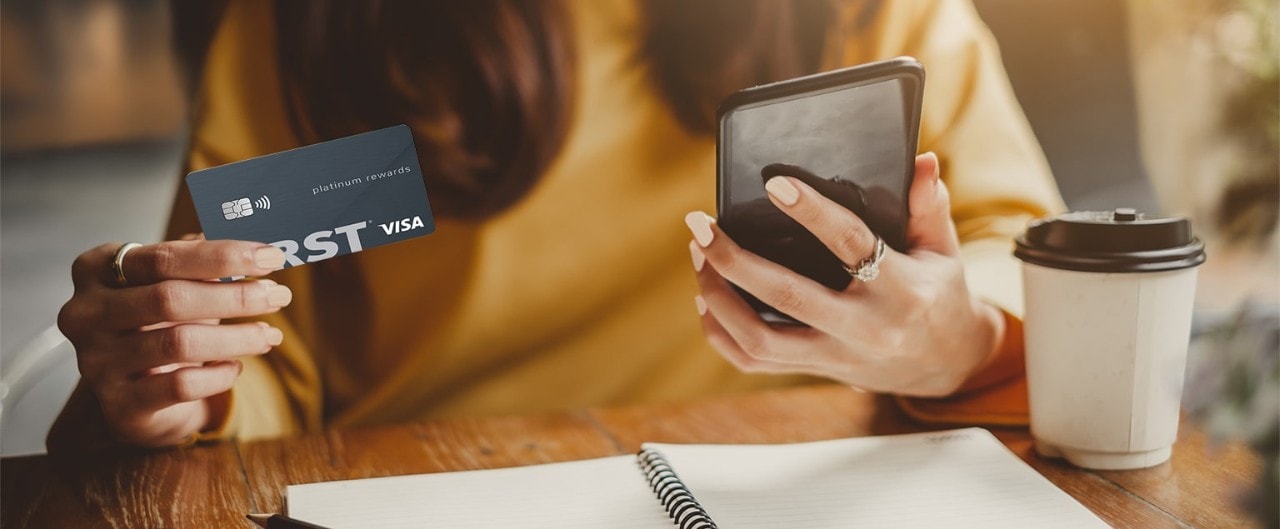 Asian woman holding First Financial credit card and looking at smartphone