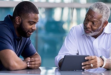African-American father and adult son reviewing information on a tablet